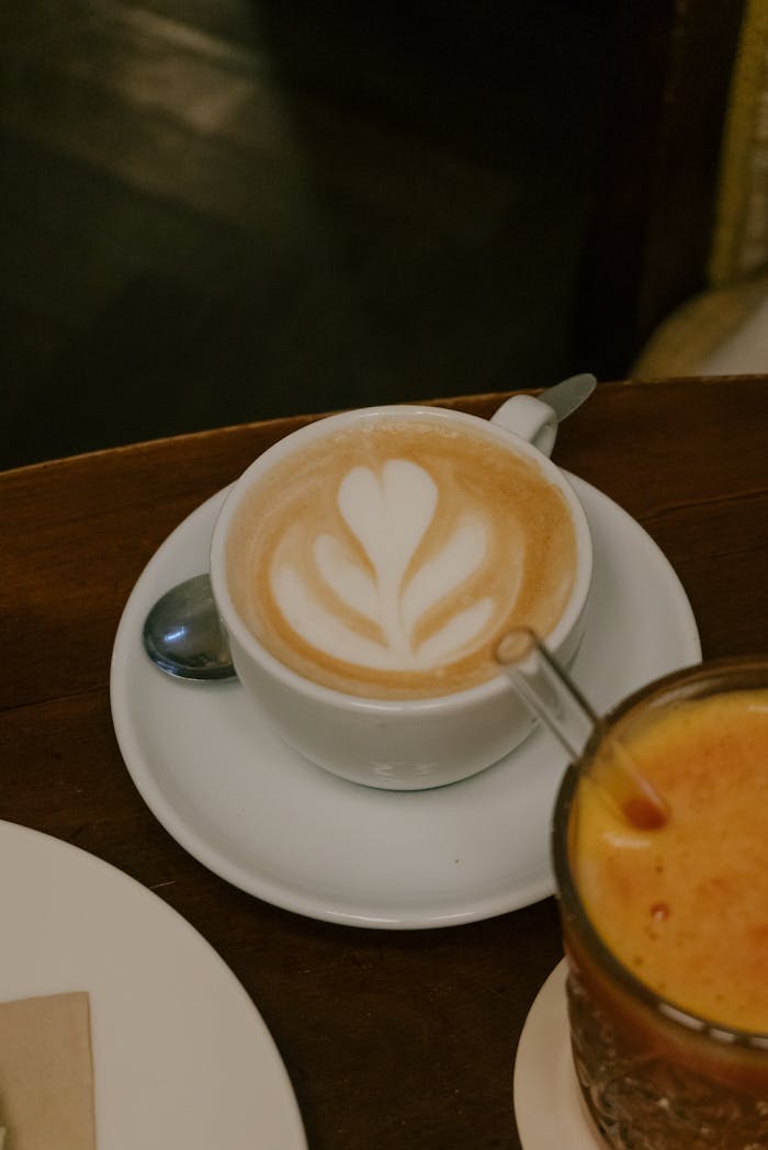 A beautifully crafted latte with latte art, accompanied by a glass of fresh juice on a wooden table.