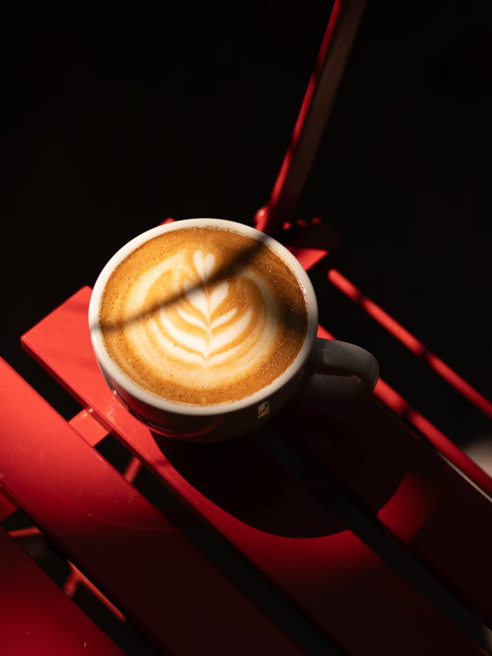 Capture of a beautifully crafted latte with intricate foam art on a vibrant red table.